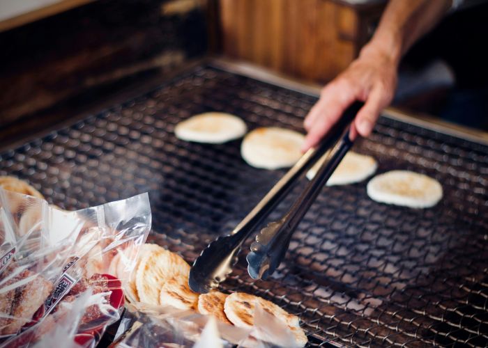 A man is grilling senbei rice cakes on a grill, placing the prepared senbei in a row.