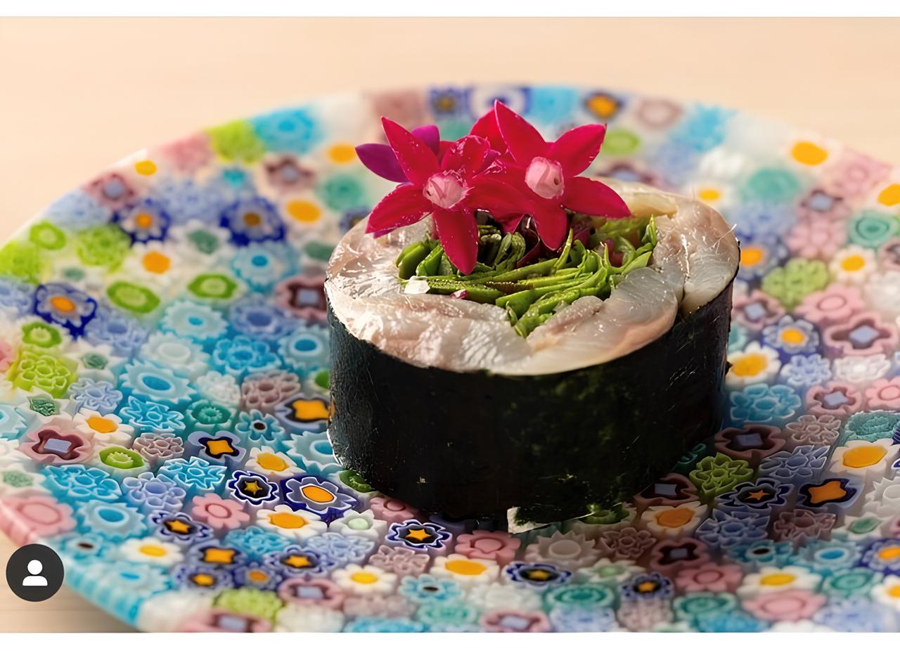 Intricate sushi roll with vibrant flowers and seaweed garnish