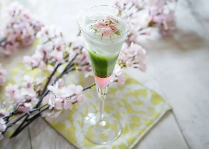 A green mocktail is set against a background of cherry blossom table decorations.