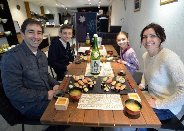 Guests at a nigiri sushi-making class, smiling at the camera. In front of them, plates of sushi sit on the table..