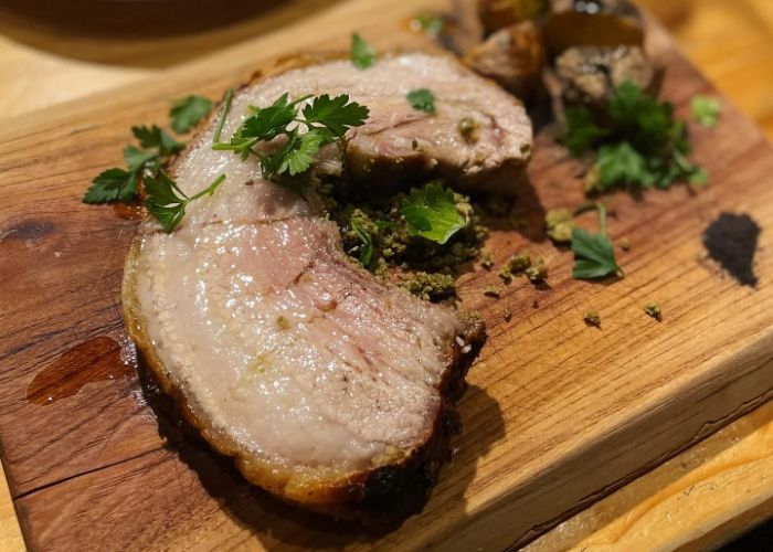 A juicy cut of meat at falo, served on a wooden board and garnished with herbs.