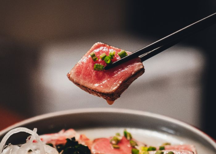 Raw sashimi being picked up from a bowl by wooden chopsticks.