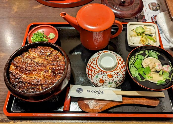 An eel set meal at Unafuji, including grilled eel over rice, herbs, spring onions, and tea.