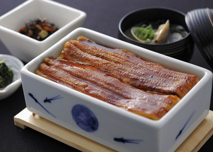 A serving of eel served in a rectangular porcelain bowl at Mame-tanuki, coated in the famous eel sauce.