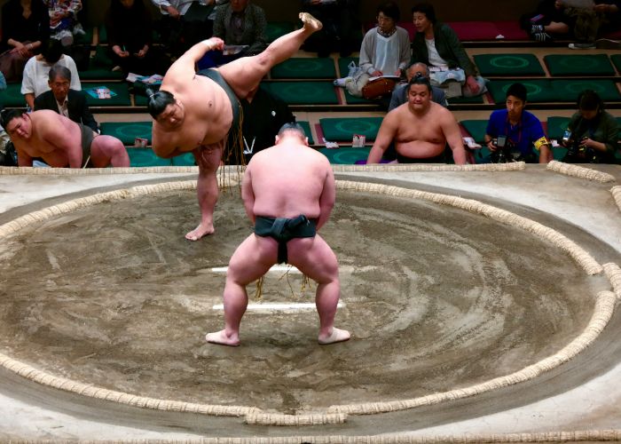 Two sumos in the ring, with one about to slam his foot down with force.