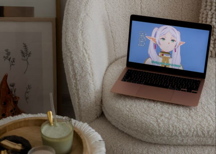 A laptop resting on a chair. The screen is showing the ending credits for Frieren, an anime featuring an elf with silver hair.