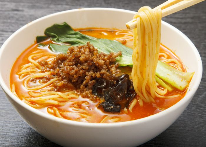 A bowl of tantanmen. Chopsticks are picking up some noodles from the spicy looking broth.