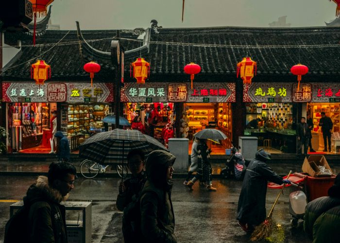 A busy street in China, as people walk through the rain in front of neon signs and lit paper lanterns.