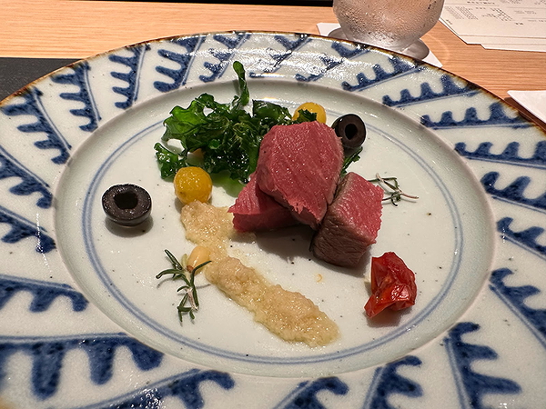 Gourmet dish with beef, greens, and olives on an elegant plate