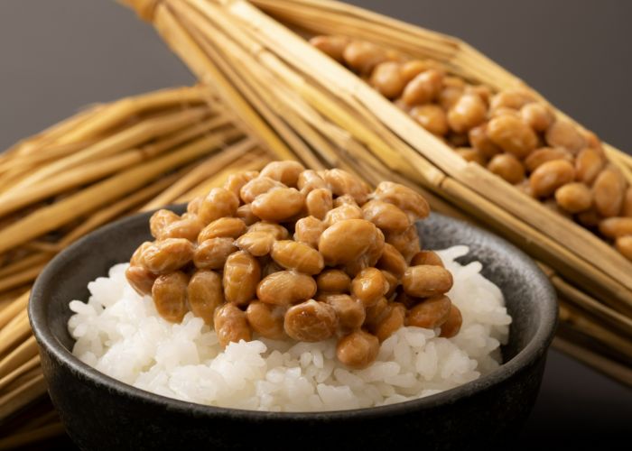 A serving of natto over rice, with straw-wrapped natto in the background.
