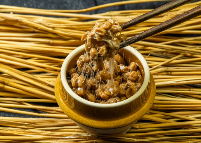 Natto being picked up with chopsticks, leaving behind a sticky residue.