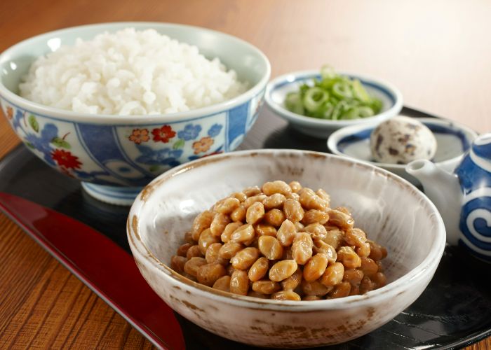 Natto served in a bowl alongside a Japanese set meal of rice, egg, and spring onions.