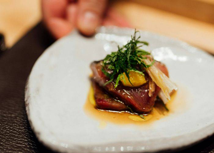 A chef handing a small dish with a garnished sushi dish.