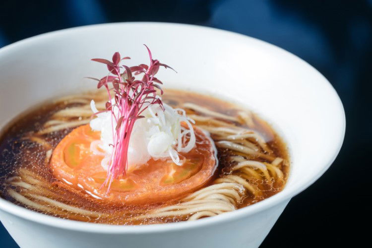 A slice of tomato lay on a bed of ramen noodles and garnished with toppings at Vegan Ramen Uzu Kyoto.