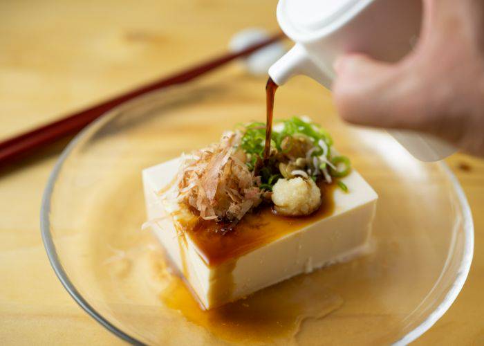 Soy sauce being poured onto a chilled block of hiyayakko.
