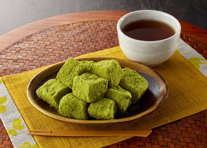 A plate of matcha warabi mochi with a cup of tea beside it