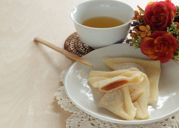 A plate of yatsuhashi with a cup of tea and flowers beside it