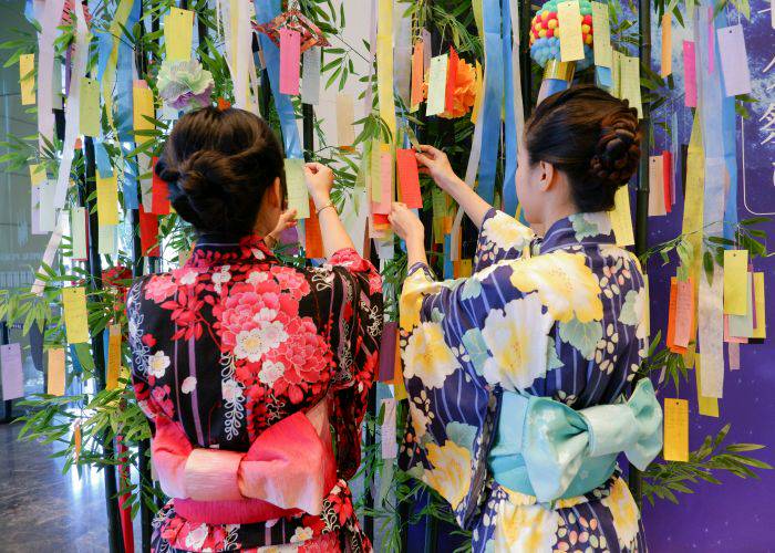 Two women in kimonos adding their wishes to a Tanabata tree.