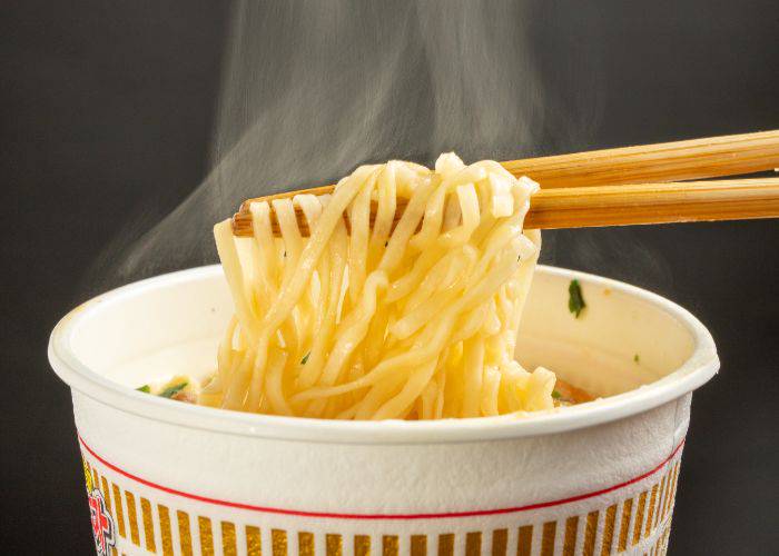 Chopsticks pulling out steaming noodles from a cup of instant ramen