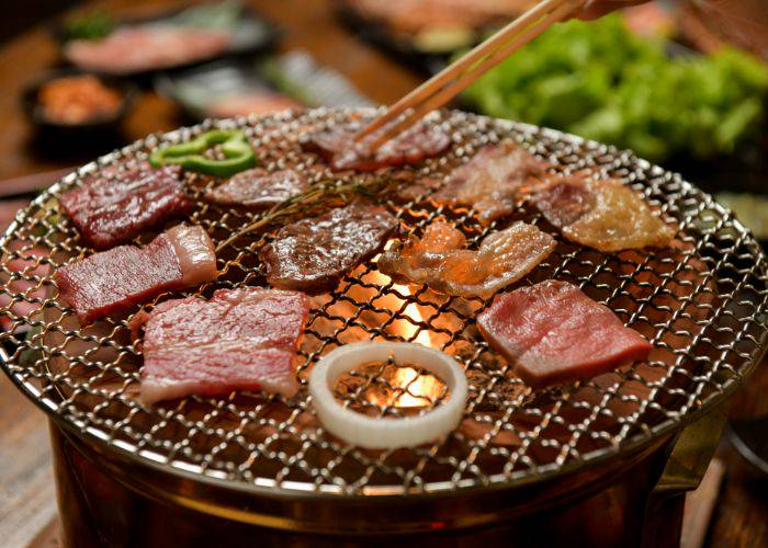 Meat and seafood grilling over charcoal on a round yakiniku grill.