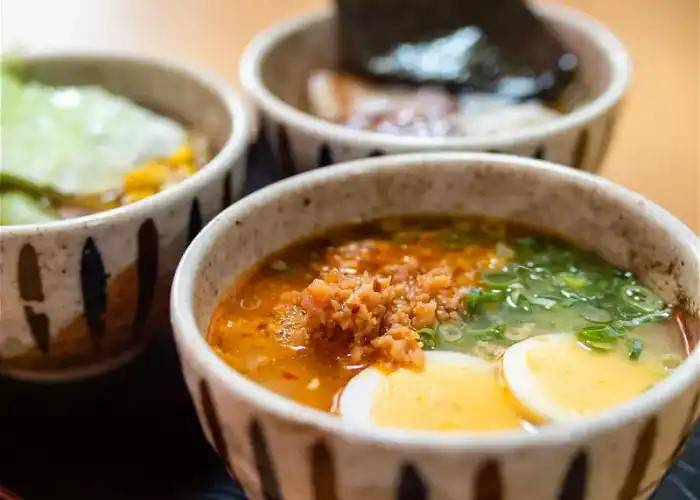 A bowl of homemade ramen, featuring a boiled egg, spring onion, mince, and side dishes.