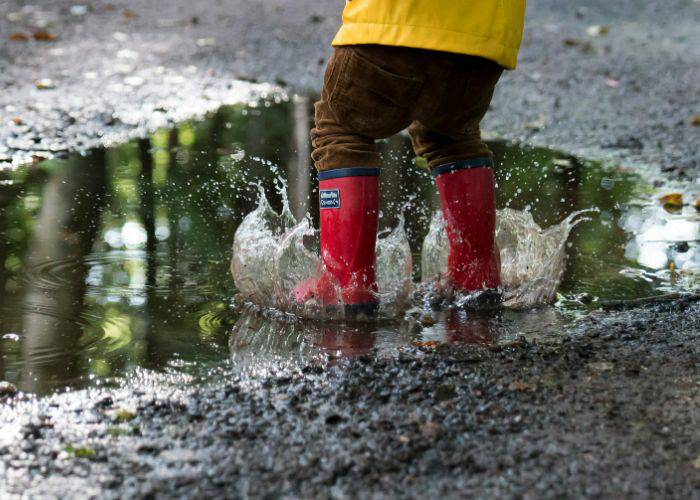 A child in red rainboots jumping in a puddle.