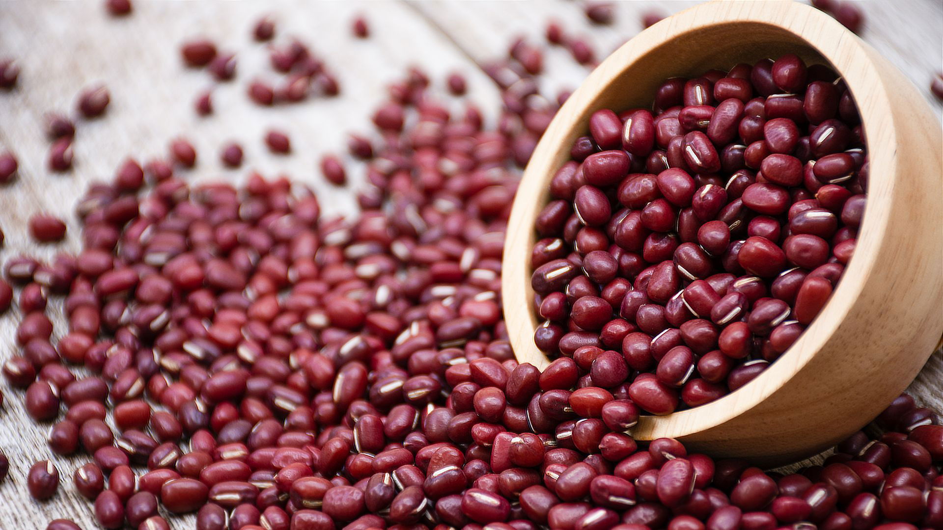 Red adzuki beans spilling from wooden bowl on rustic table
