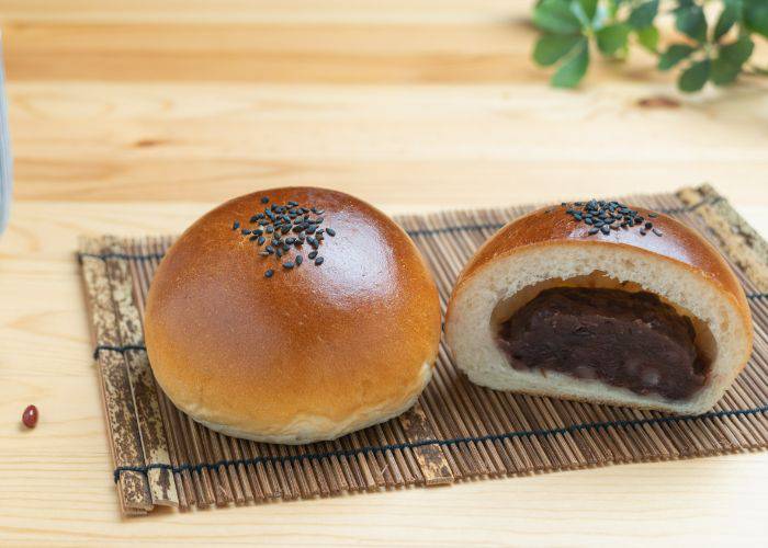 A Japanese red bean bun (anpan) on a bamboo serving tray, One is cut in half to reveal the red bean paste inside.