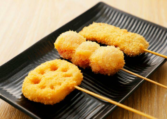 A selection of deep-fried skewers served up on a ceramic serving tray.