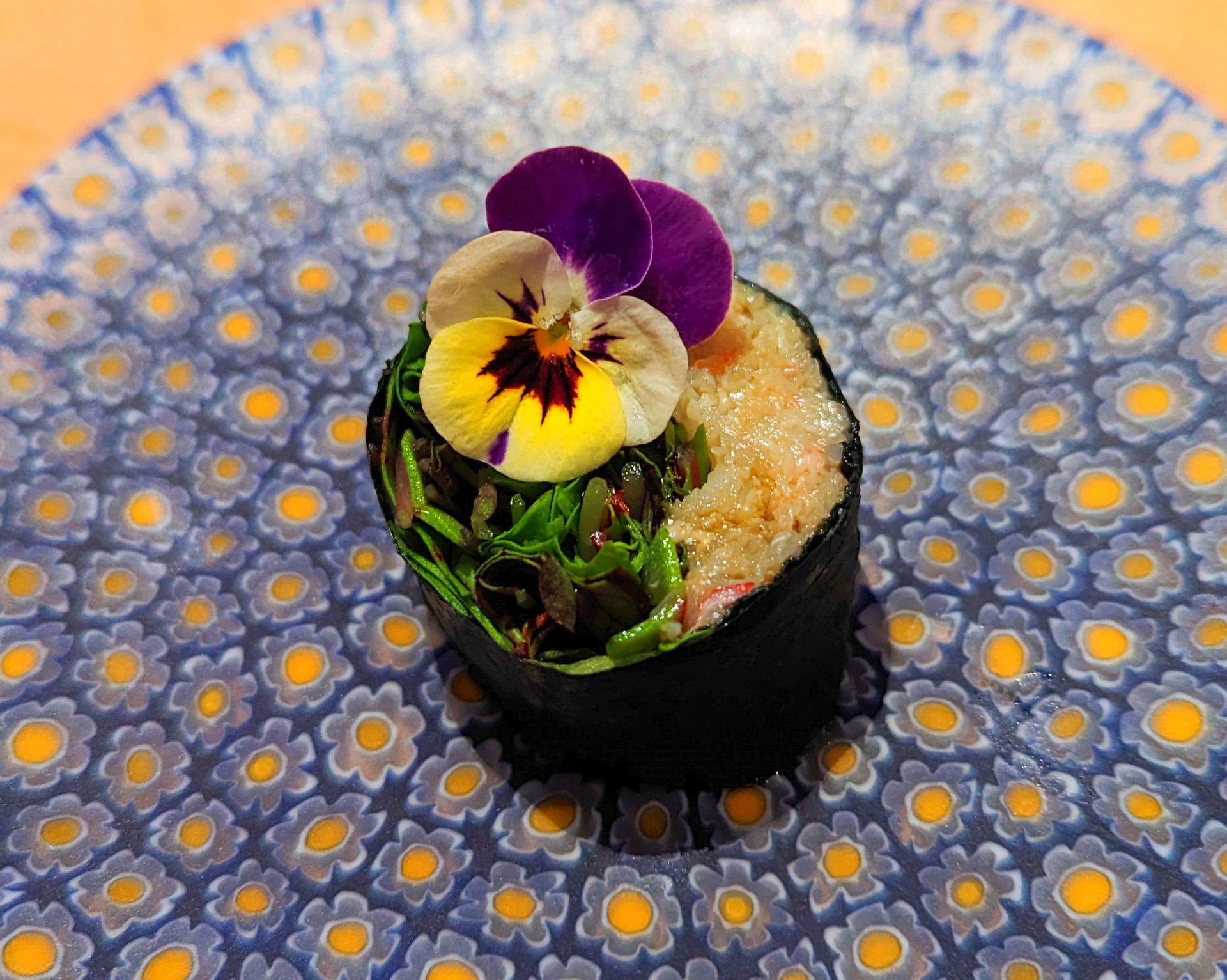 Gourmet sushi roll with edible pansy on decorative plate