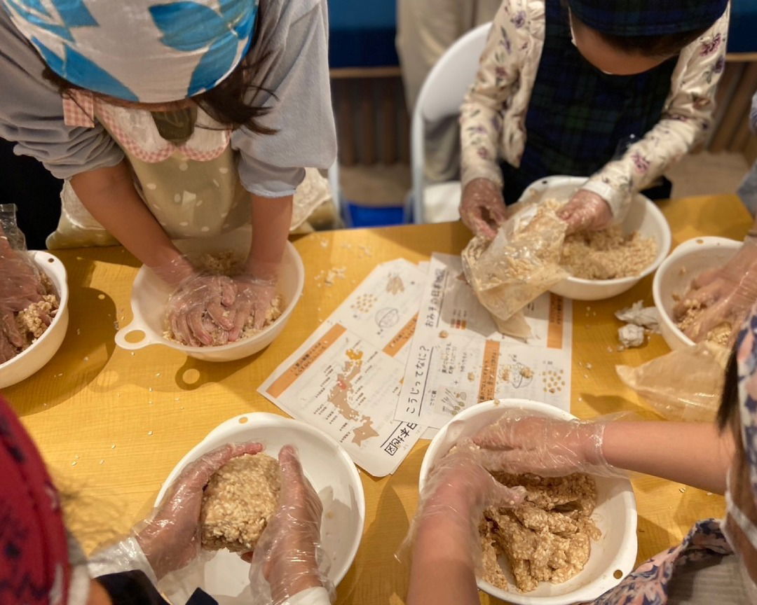 Guests wearing gloves working on making miso paste in bowls.