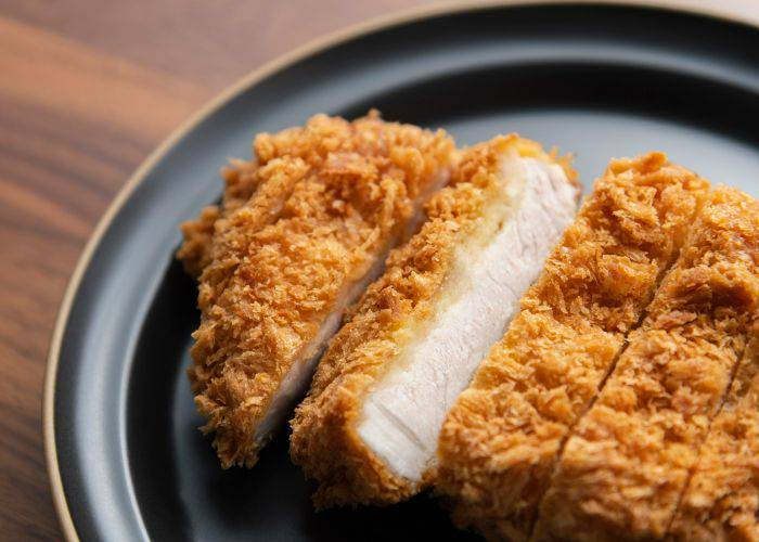 Sliced tonkatsu pork cutlets on a plate. Cooked pork inside a golden breadcrumb coating.