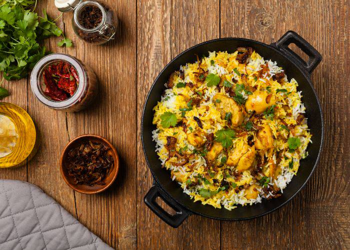 A top-down shot of a biryani dish of chicken, vegetables and rice on a wooden table.