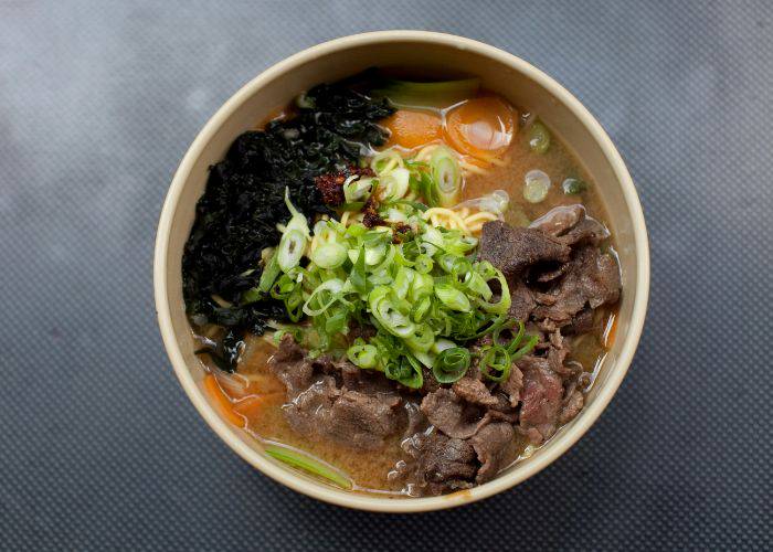 A top-down shot of ramen in a bowl, filled with broth, noodles, seaweed, carrots, spring onions and beef.