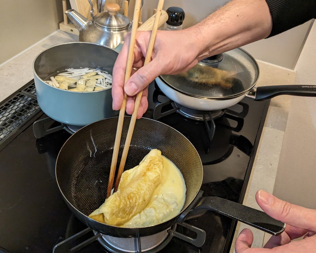 Making a Japanese rolled omelet in a small pan at a home cooking class in Tokyo