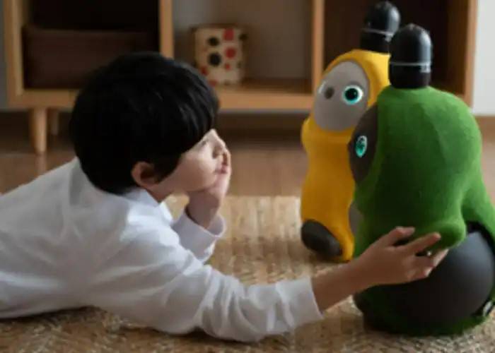 A boy lying on a rug, stroking his LOVOT robot.