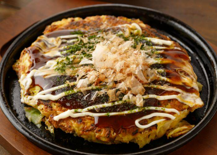 A traditional Japanese okonomiyaki cabbage pancake, smothered in sauce and bonito flakes.