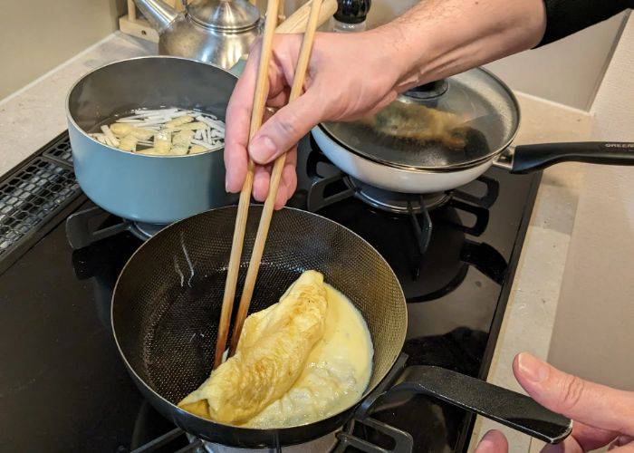 Someone using chopsticks to create a Japanese omelet in a frying pan.
