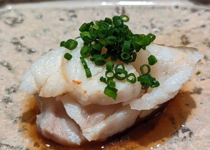 A serving of sashimi at Ajuta, soaked in soy sauce and garnished with spring onion.