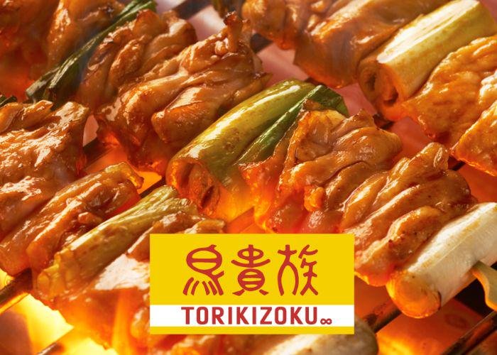 Glistening skewers of meat grilling over charcoals with the Torikizoku logo overlaid on top