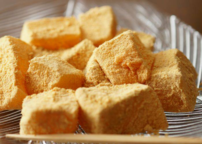 A close-up shot of warabi-mochi in a glass bowl, well-dusted with kinako powder.