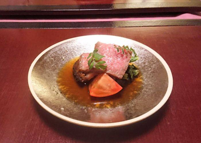 An elegant dish at Kikusaiko, featuring a small portion of meat and vegetables in a sauce.