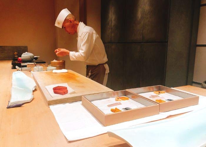 Omakase sushi chef dressed in white preparing sushi for guests