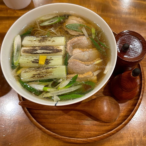 Delicious ramen bowl with sliced pork and grilled leeks on wooden table