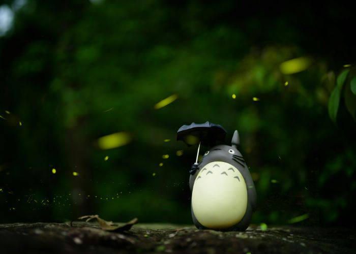 A figure of Totoro holding his umbrella as real-life fireflies fly around him.