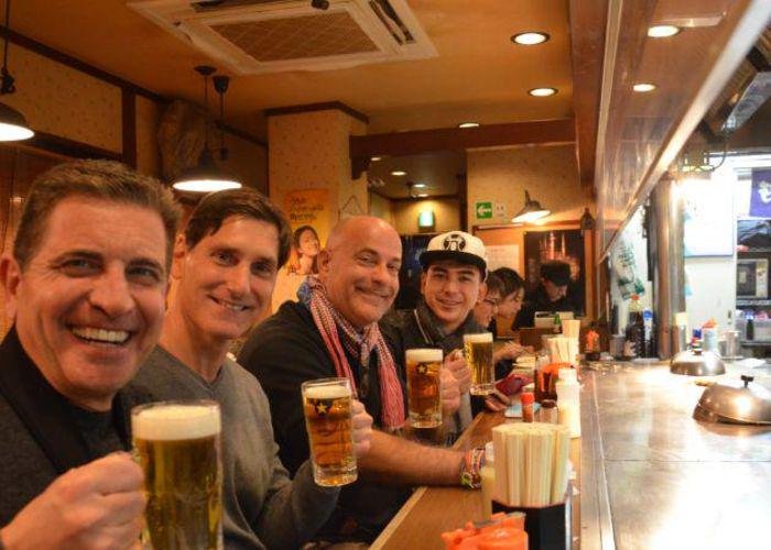 Smiling men raising glasses of beer at a teppanyaki restaurant in Shibuya during a food tour