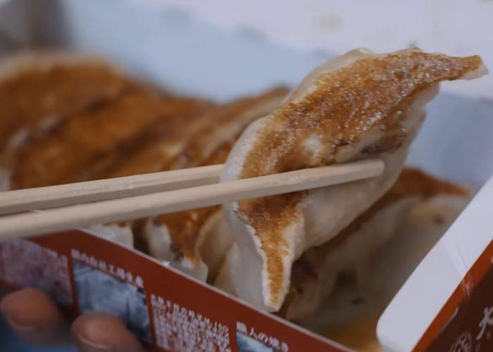 Chopsticks picking up a single gyoza, crispy on one side and doughy on the other.