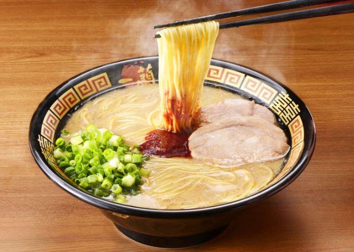 Bowl of Ichiran Ramen, one of the best ramen in Tokyo, with a spicy red sauce in the center of thin noodles in a tonkotsu broth, with a pop of green from the chopped scallions and thinly-sliced chashu pork.