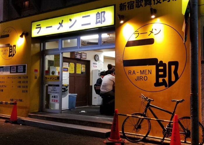 Exterior of Ramen Jiro Shinjuku Kabukicho, glowing yellow shop sign and vibrantly yellow-painted walls, showcasing the sign "RA-MEN JIRO" 
