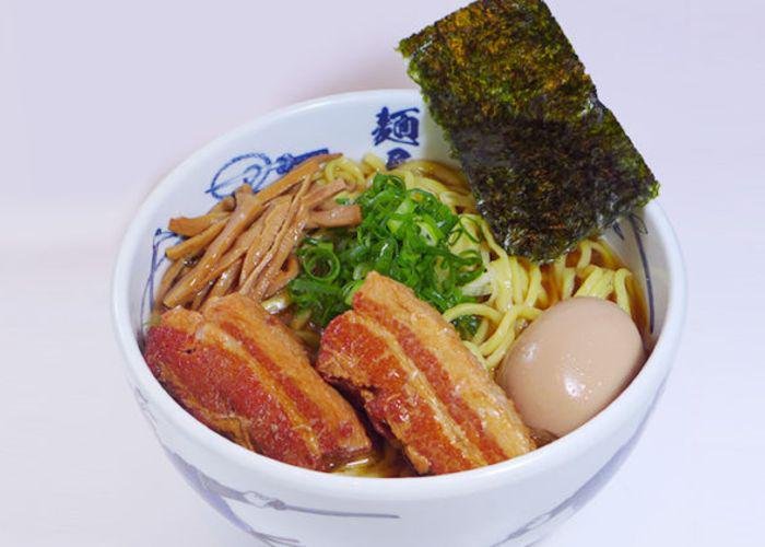 Large bowl of ramen, with huge strips of meat and an egg, from Menya Musashi against a white background